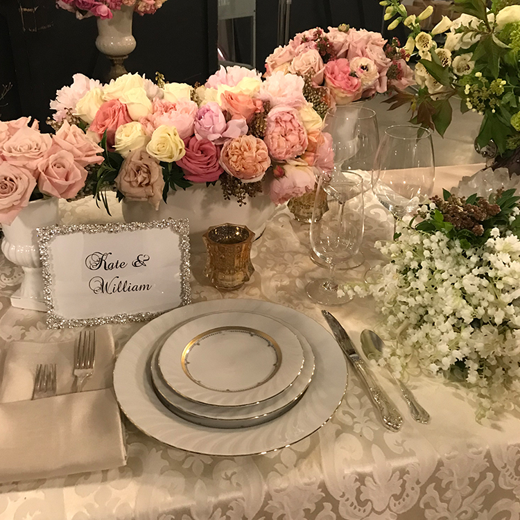 An image of the table set up with gold trim dishes and a white and pink rose floral