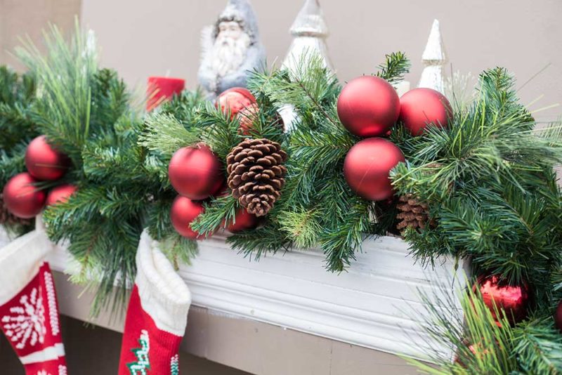An image of green garland decorated with red ball ornaments and pinecones
