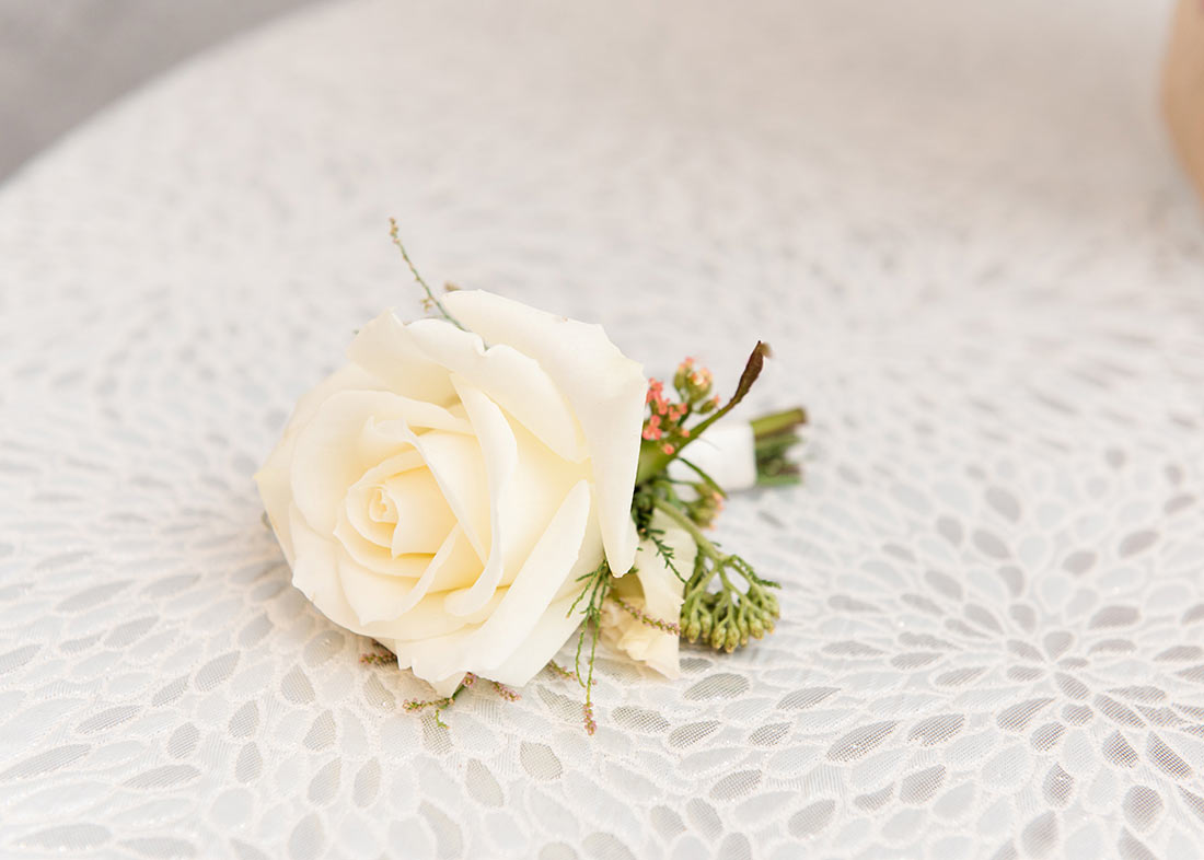 An image of a single white rose corsage laying down on white lace
